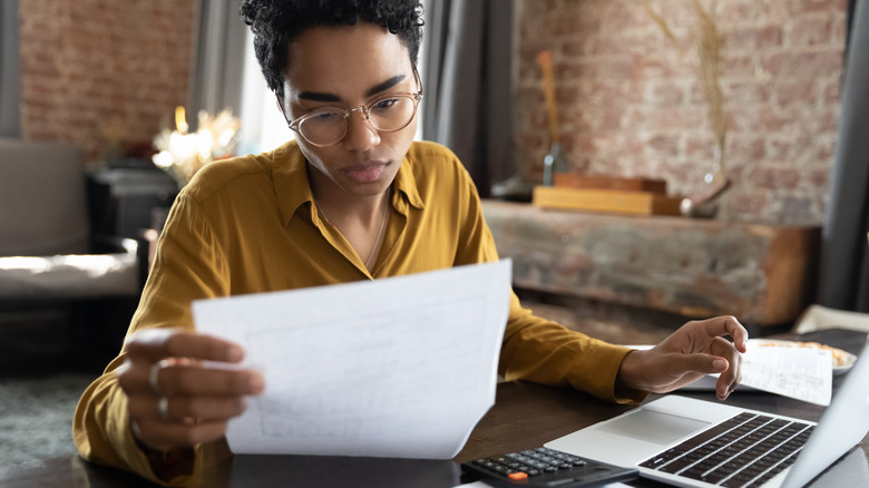 person looking at a piece of paper while sitting at desk with laptop