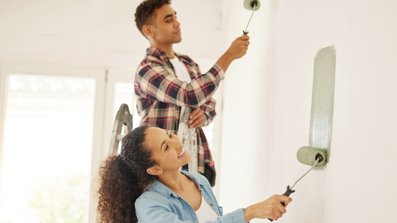 Two people using rollers to paint a wall