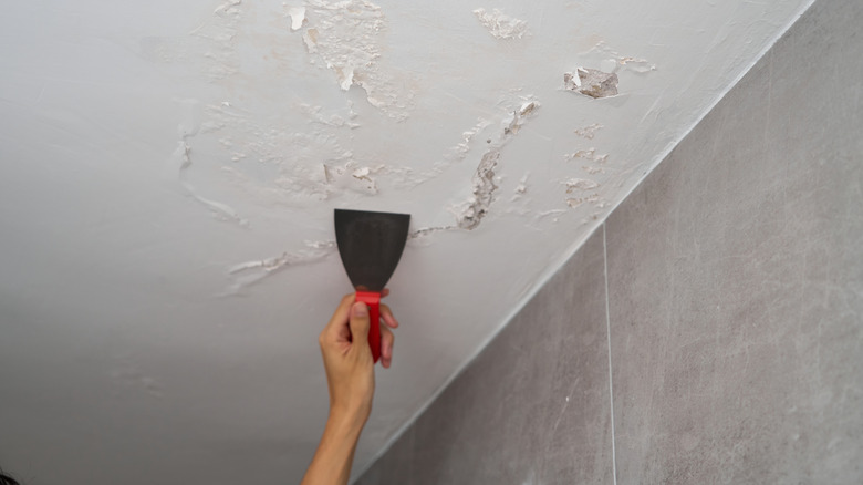 Hand scraping water damage off ceiling in tiled room