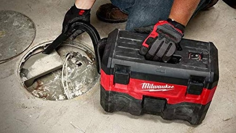 Person using a cordless Milwaukee vacuum to clean out a pit