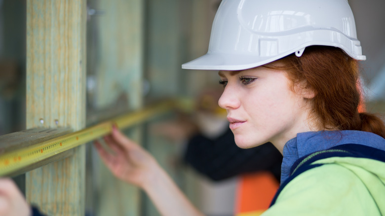 A construction worker in a hardhat measuring wood with a tape measurer