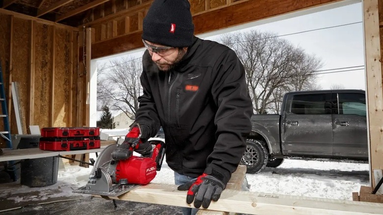 Man cutting a board in an open garage during the winter