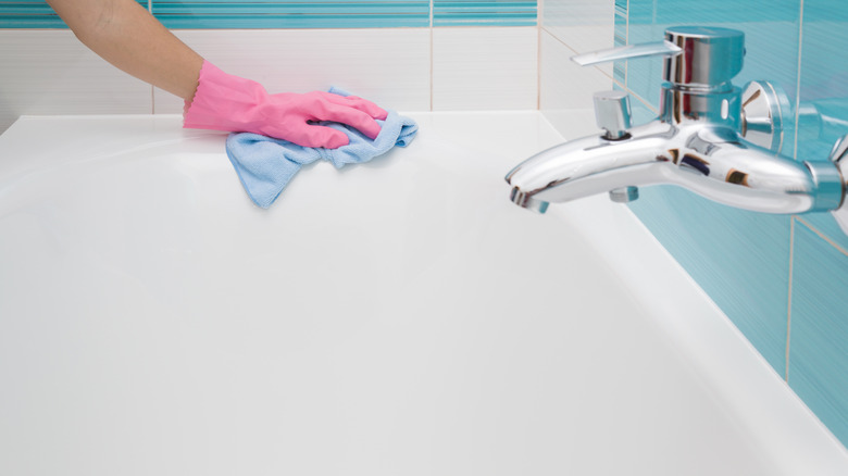 person with pink glove wiping bathtub