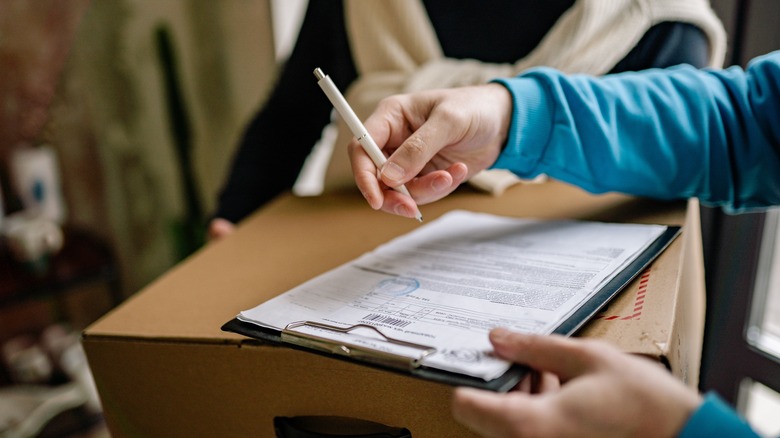 Person signing paperwork on clipboard