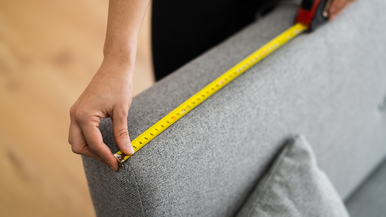 person measuring back of couch