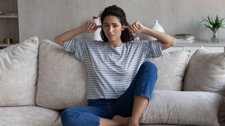 woman plugging ears on couch