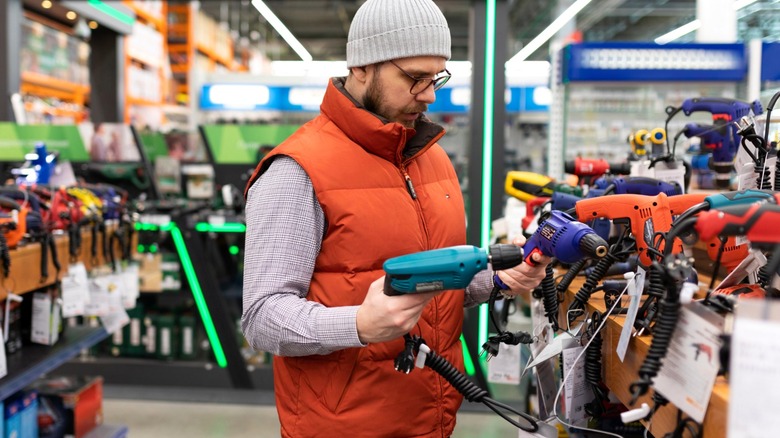 Man in orange vest comparing electric drills in home improvement store