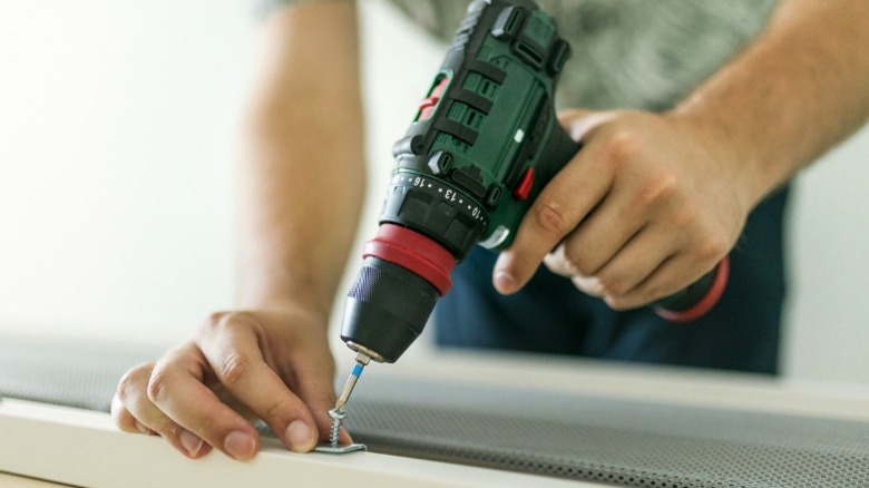 Person using cordless drill to put screw into bracket on wood frame