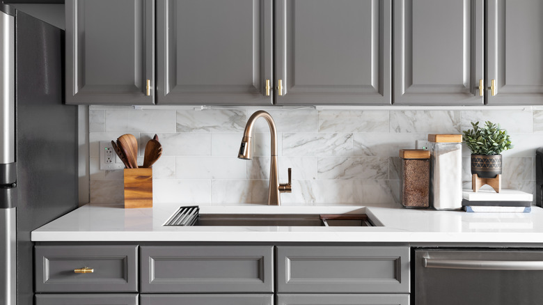 Gray kitchen cabinets with gold faucets, plants, and wood elements