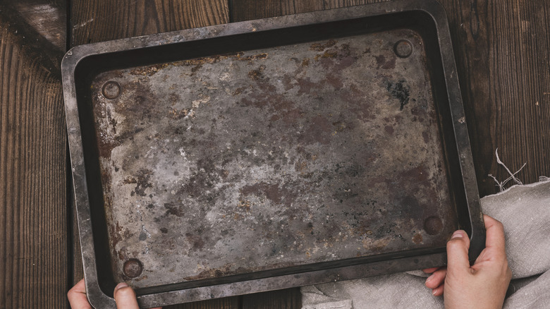 Two hands hold a dirty baking sheet over a wood surface.