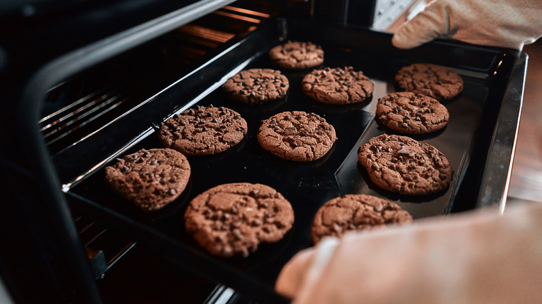 A pair of hands with oven mitts taking a fresh batch of cookies out of the oven