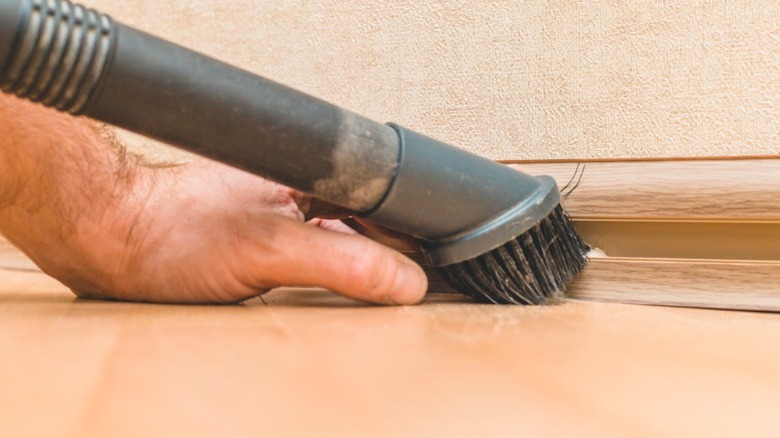 Man using a vacuum wand with a brush attachment to vacuum a wood baseboard