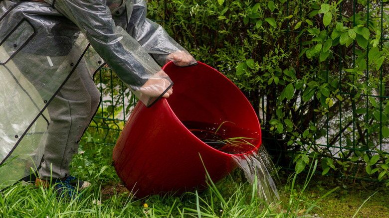 Person in protective gear pouring a bucket of water onto the ground