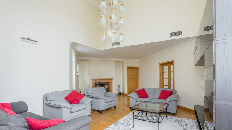 Living room with high ceilings, lighting fixture, gray couches, red throw pillows, a rug and a glass table