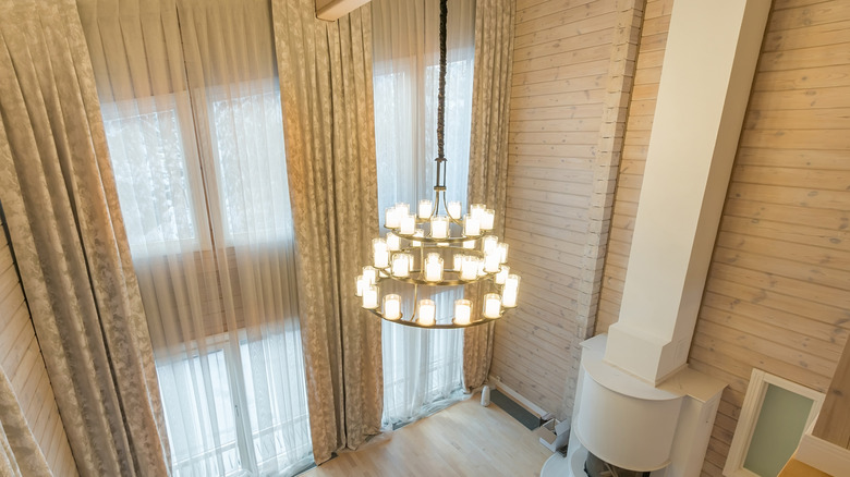 Room with high ceilings with a hanging chandelier and floor to ceiling curtains