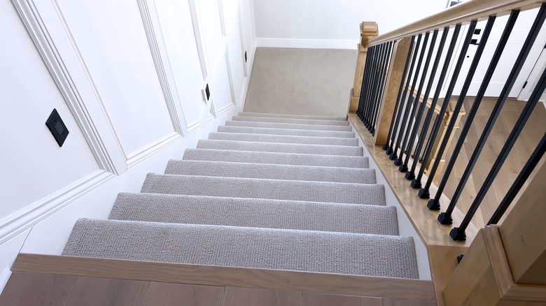 A staircase with gray carpet and a wood and black railing