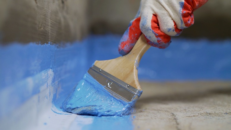 A person applies waterproofing paint to a bathroom floor