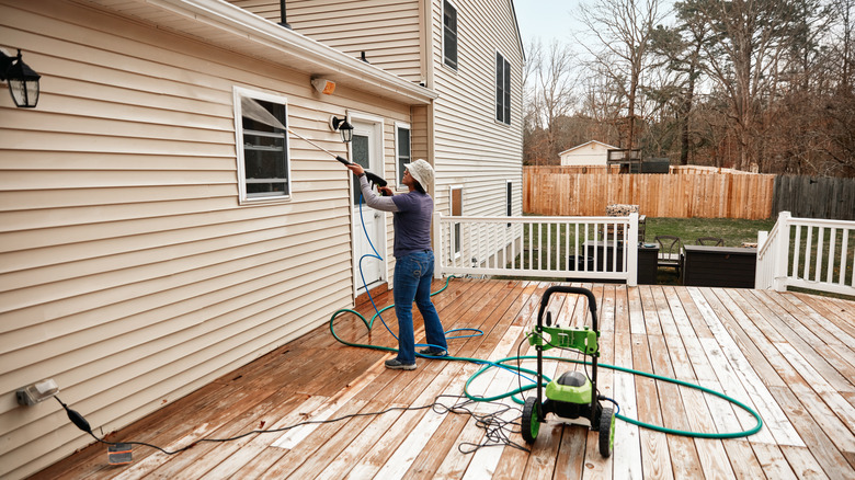 Person pressure washing siding from the top down