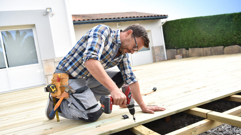 man using power drill on wood deck