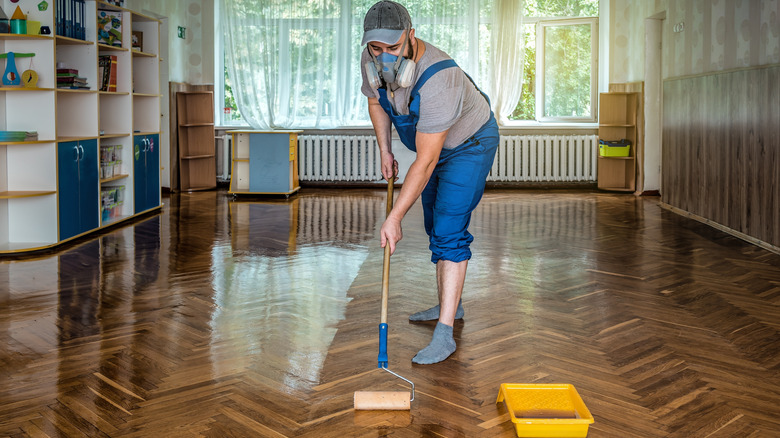 A man wearing a protective mask rolling varnish onto a hardwood floor