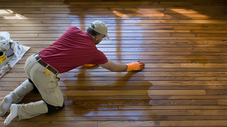 A man on his hands and knees applying stain to a hardwood floor