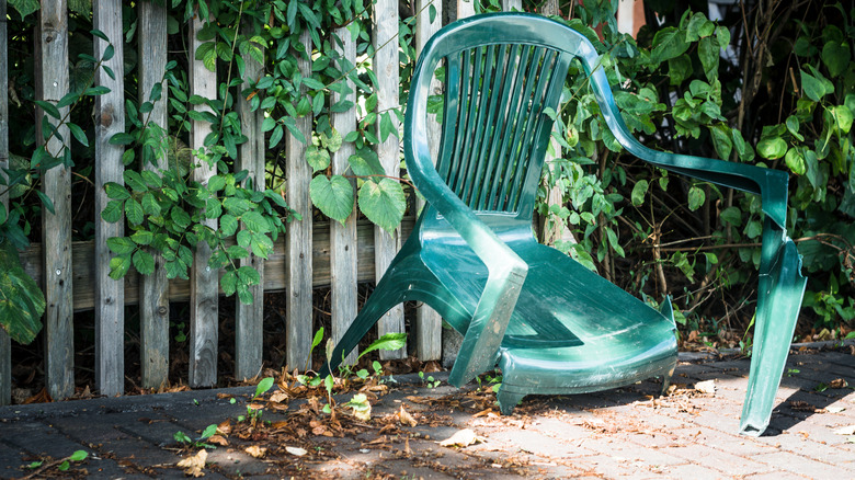 A broken plastic chair against a fence