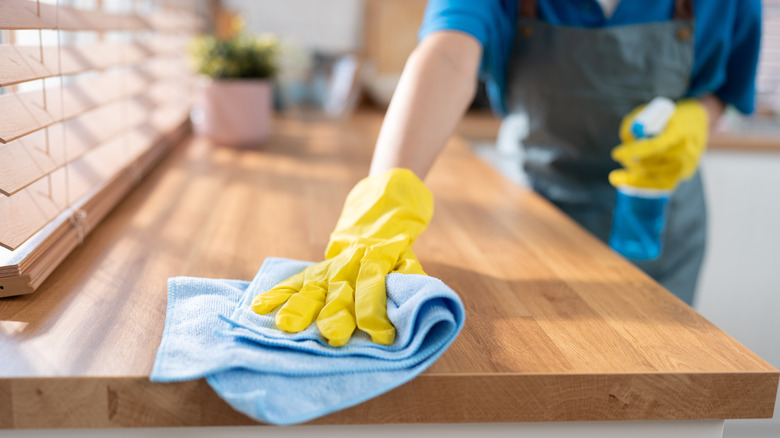 Gloved hand cleaning wooden surface with microfiber cloth