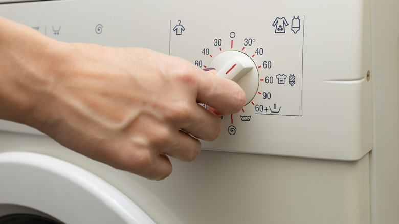 Hand turning the temperature knob on washing machine