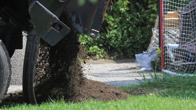 A truck drops a pile of topsoil on a lawn with no tarp in place