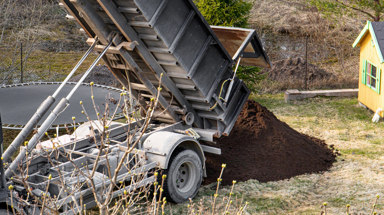 A truck unloads a large pile of topsoil onto a lawn