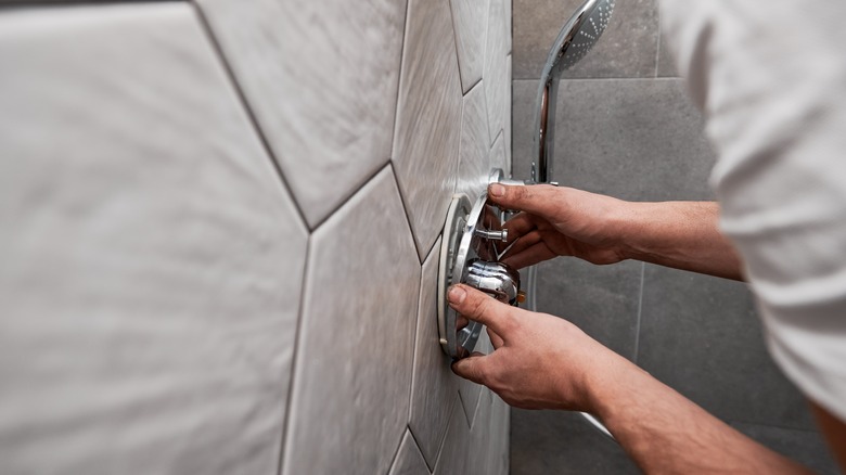 Close up of man standing by the wall with ceramic tile and installing shower faucet with metal handle in apartment