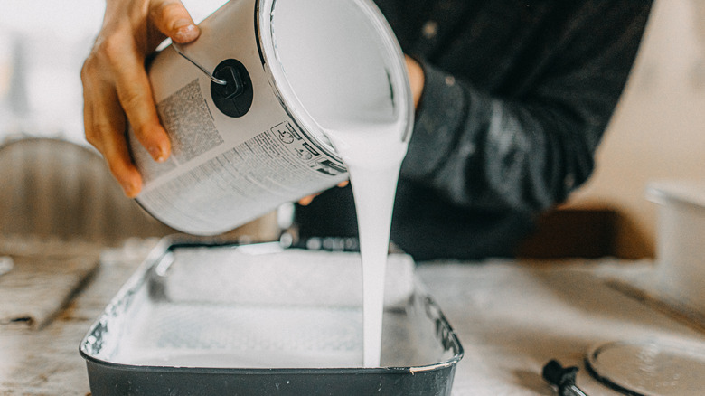 Person emptying a can of white paint