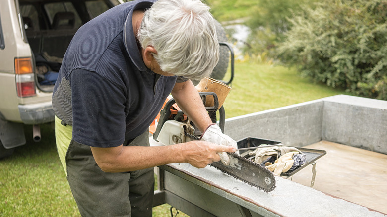 A man sharpens his chainsaw with a file