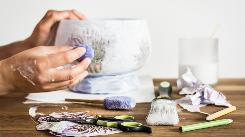 Hands decoupaging a vase with floral paper