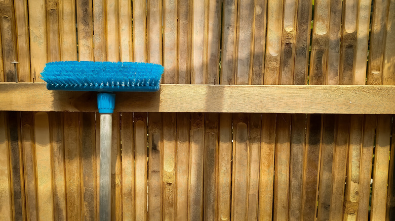 A push broom leaning against a dirty bamboo fence