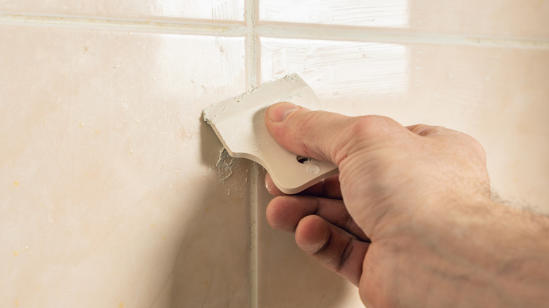 A hand using a rubber spatula to press grout between tiles