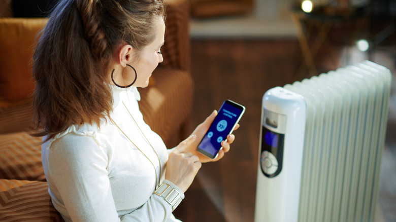 A woman using smart technology on her cellphone to set up her space heater