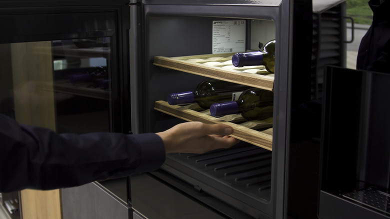 A person taking a bottle of wine out of a wine fridge