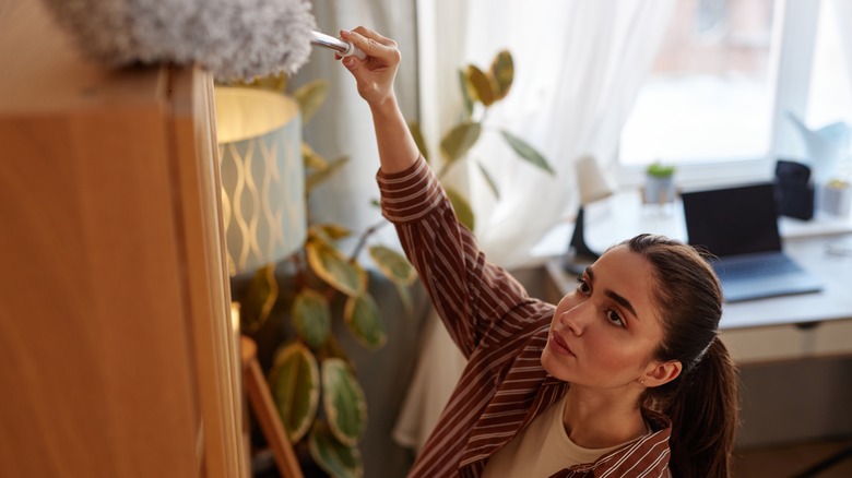 A woman dusts the top of a tall shelf