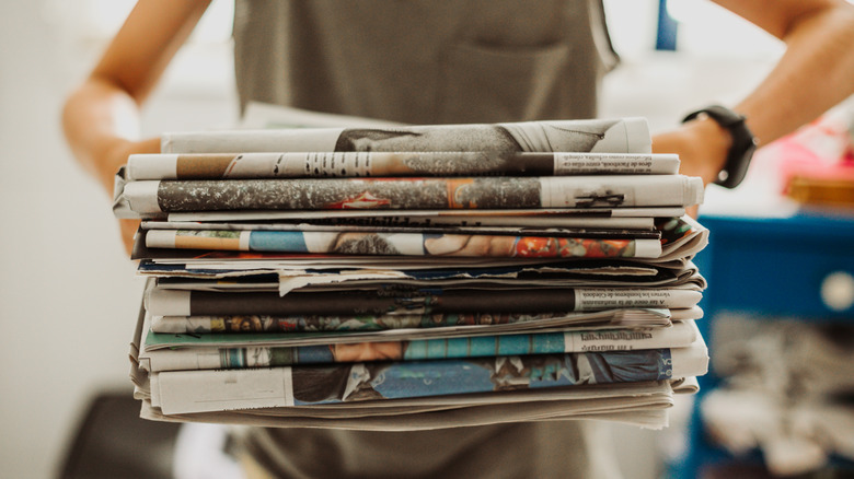 A person carries a stack of old newspapers