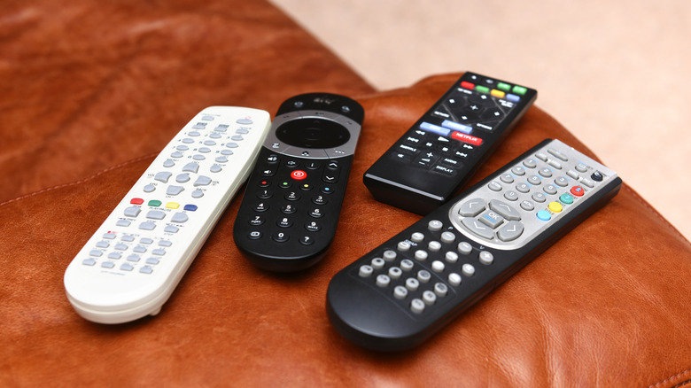 Four remote controls, each a different size, sit on an orange couch