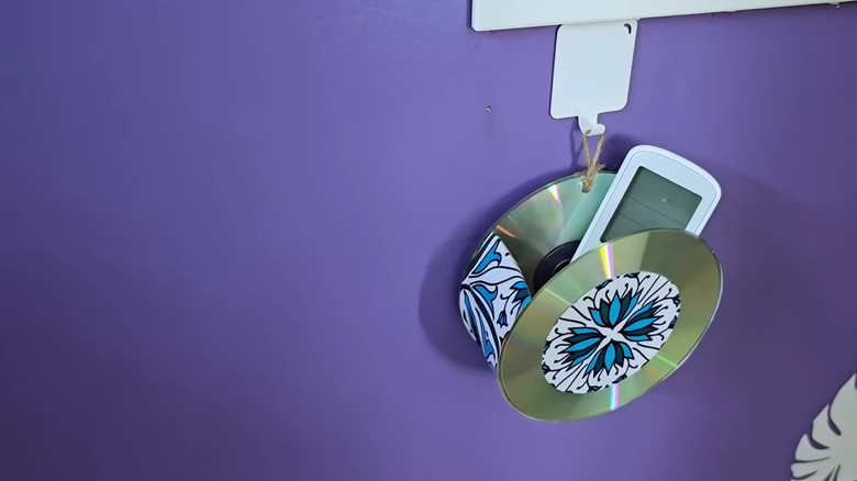 A fan remote sits inside of a remote holder made of two CDs hung on a purple wall