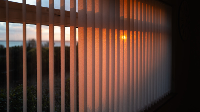 Shallow focus on vertical window blinds with a golden glow as the sun sets