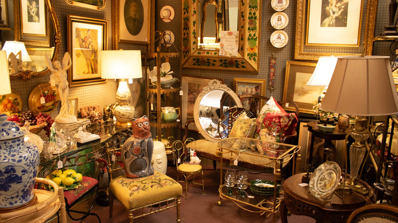 An antique store features vintage chairs, mirrors, lamps, and statues