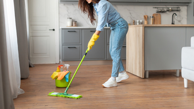 A woman cleans wood flooring with a mop.