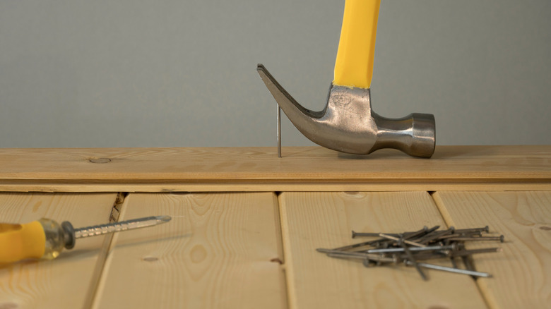 A pile of large nails beside a hammer and wood