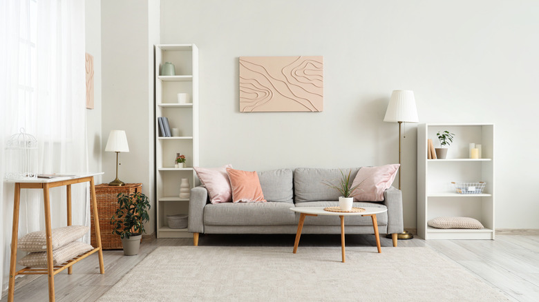 A large minimalist living room with grey and pink accents and a  clutter-free shelves and floor.