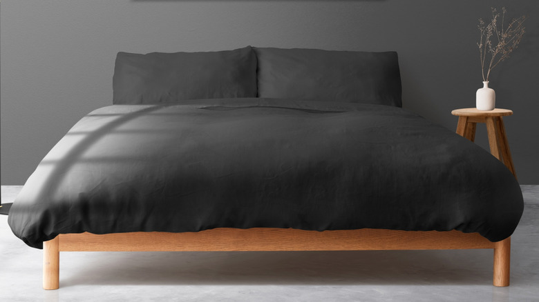 A minimalist bedroom has dark walls and bedding and no headboard