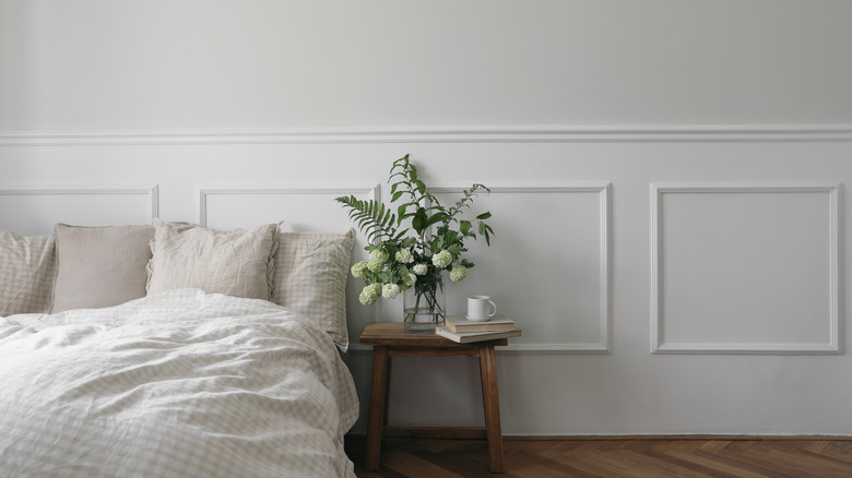 Wall moulding is used as a headboard alternative in a white bedroom