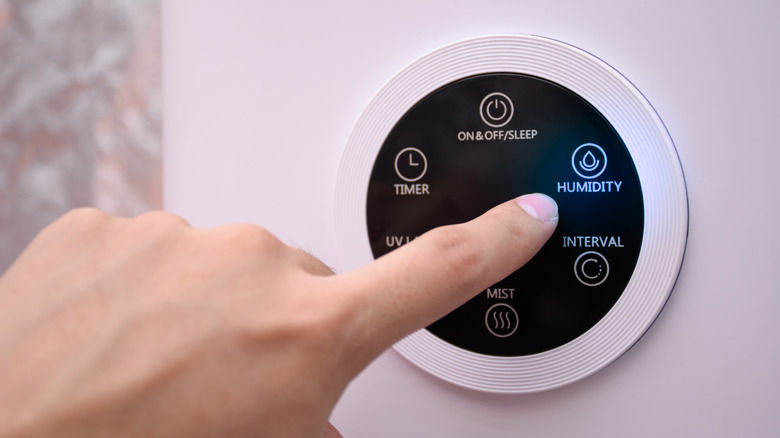 a finger presses the Humidity icon on a wall-mounted touchscreen control panel